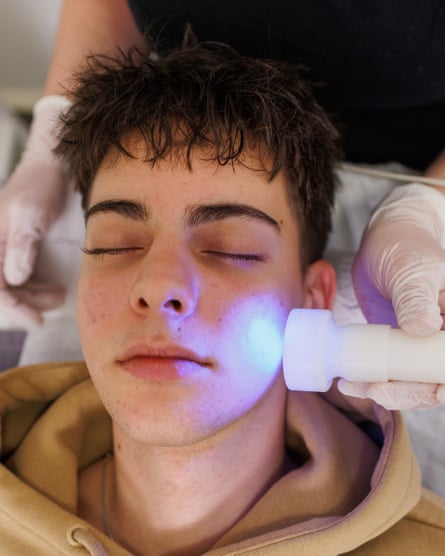 A beauty therapist administering blue-light therapy on a teenage boy.