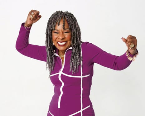 Martha Reeves wearing a pink jumpsuit with white stripes, holding her hand in the air