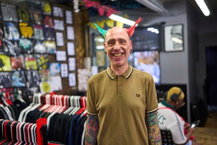 Middle-aged man with hair on the side of his head spiked up, also coloured green and red, in his tattoo shop