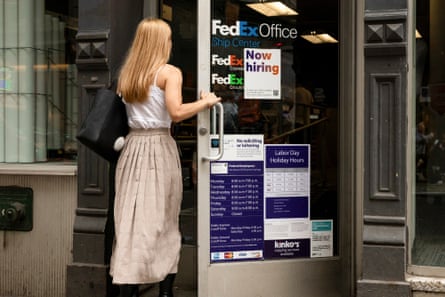 woman opening door to a fedex office with sign in window saying ‘now hiring’