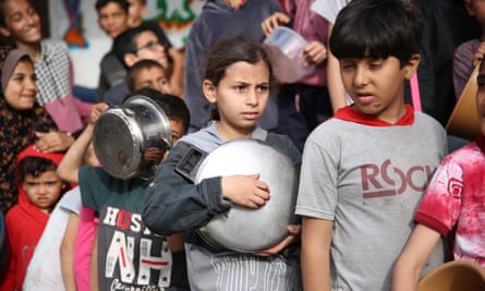 Palestinian children queue while holding empty bowls