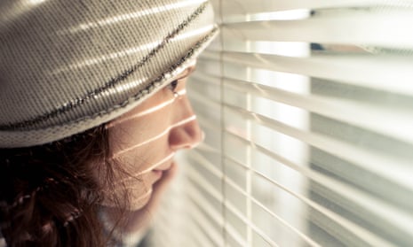 Teenage girl looking through window with blinds down