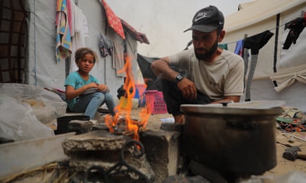 A man preparing a meal over an open fire in a displacement camp in the al-Mawasi area.
