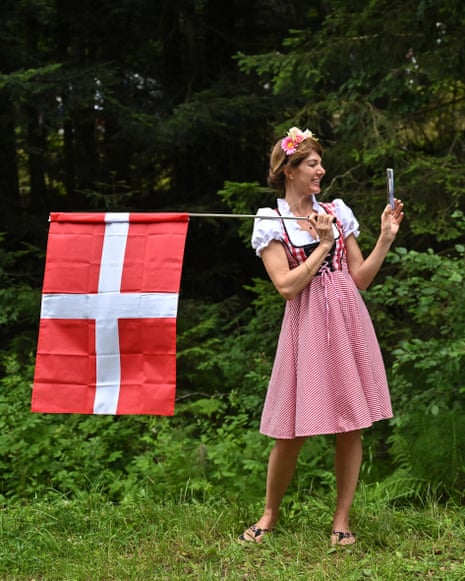 A spectator wearing traditional attire holds a Danish national flag along the race route.