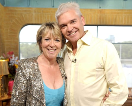 A silverhaired man smiling broadly with her arm round a woman also smiling with blond bobbed hair wearing a sky blue dress and a sparkly jacket