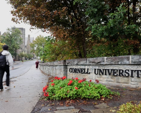 A student walks by a sign at the entrance of Cornell University