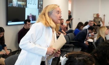 a woman in a white coat speaks in a meeting