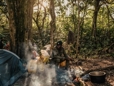 A ranger sits next to a campfire in daylight