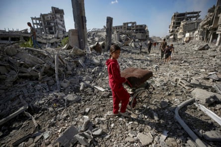 Girl pushes wheelbarrow over rubble.