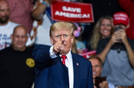 Donald Trump points a finger out to the camera as supporters behind him hold 'Save America!' signs.