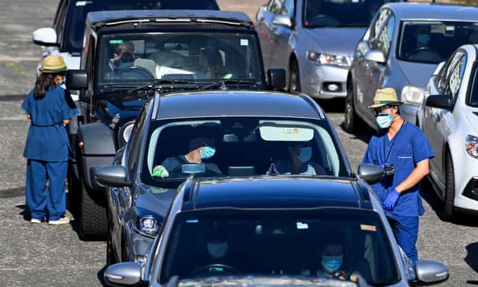Health care workers collect information from members of the public as they queue in their cars for a COVID-19 PCR test 