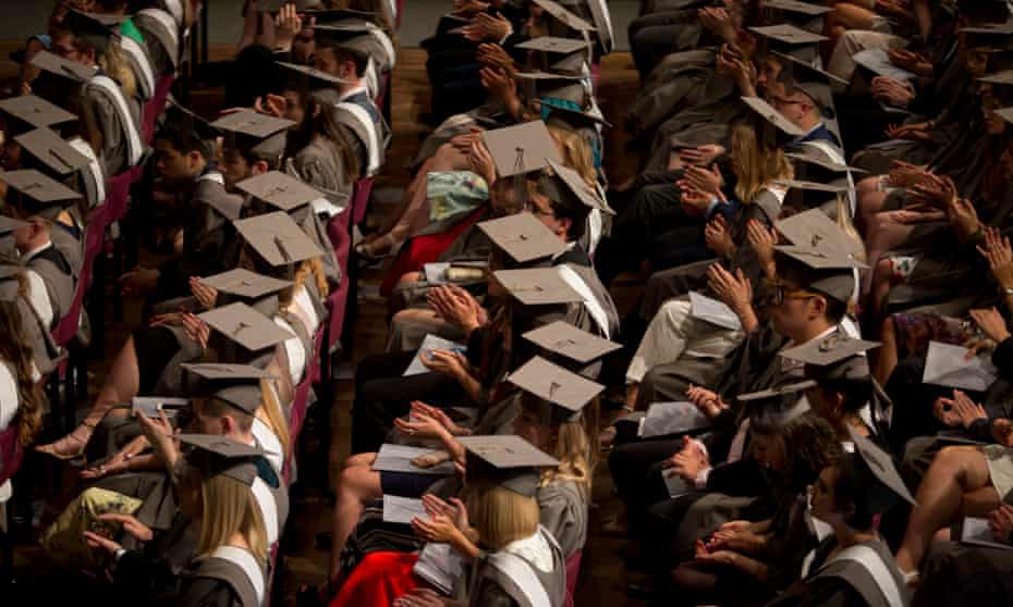 Students wearing gowns and mortarboards applaud during at their graduation ceremony.