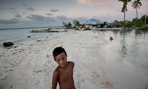 A young boy stands on a narrow strip of land that prevented his home from being drowned amid rising water levels in Kiribati.
