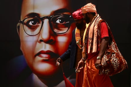Two Indian men pass a poster of a spectacled Indian man