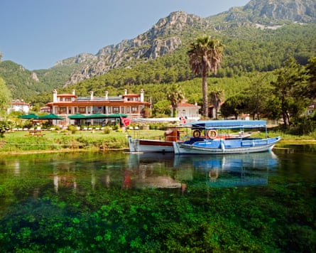 Boats on a river, with a low-rise hotel building and wooded mountains behind