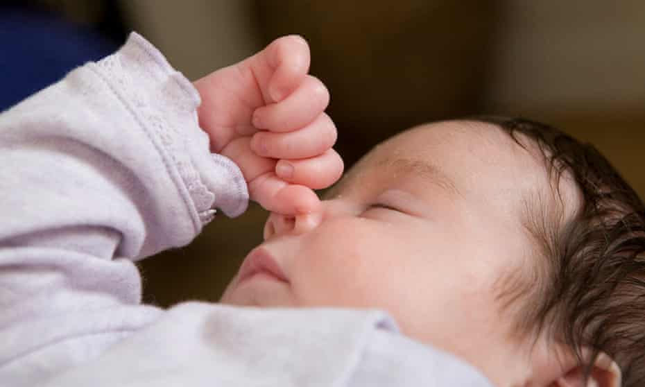 A baby girl rests her hand on her face whilst sleeping.