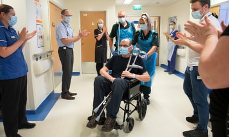 A man in a wheelchair being wheeled out of hospital past applauding staff.