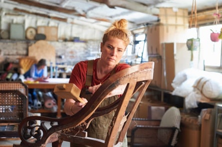 An upholsterer working on a chairShe is removing old tacks from the frame