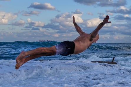 A man wearing swimming trunks dives into a foamy sea.