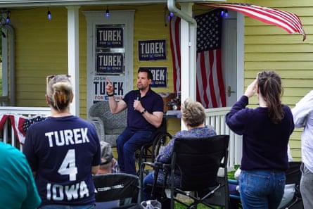 A man in a wheelchair speaks to a group of people outside a house plastered with campaign posters.
