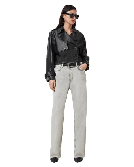 A model wearing a black leather cropped trench coat and grey denim jeans