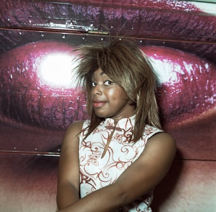 A woman in a gold wig pictured standing by some pink lips