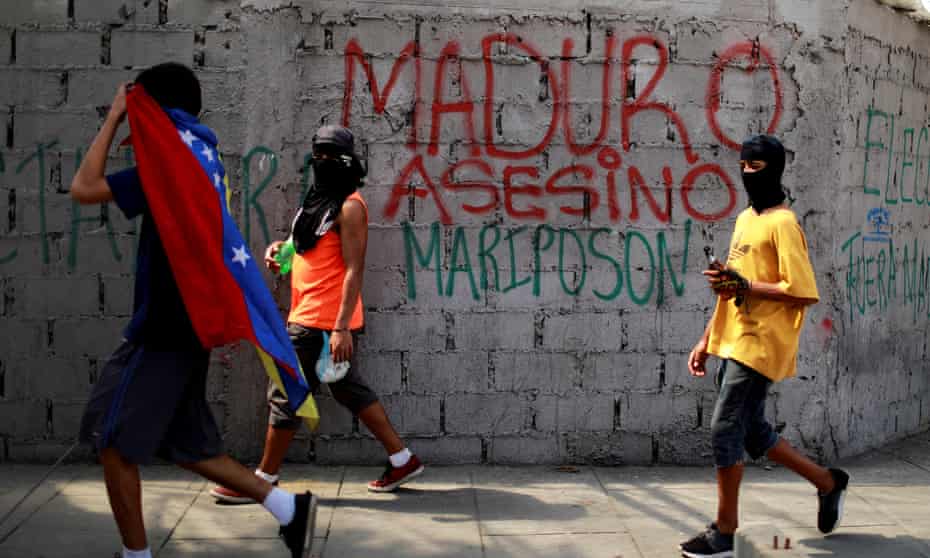 Demonstrators walk past graffiti that reads ‘Murderer Maduro’. Washington could widen the sanctions if Sunday’s vote goes ahead as planned.