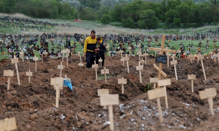People stand amid newly-made graves at a cemetery in the course of Ukraine-Russia conflict in the settlement of Staryi Krym outside Mariupol, Ukraine May 22, 2022.