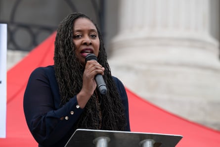 Dawn Butler speaks at an event in Trafalgar Square, standing in front of a white stone column and a red flag or awning.