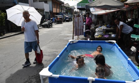 A pedestrian holding an umbrella walks past children cooling off on a makeshift pool along a street in Manila