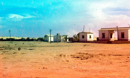 Blue and pink tinted photograph of outbuilding structures in a barren plot of land