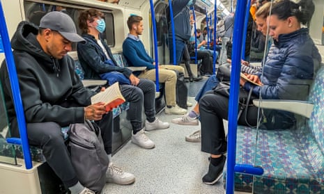 People, only a few of whom wear face masks, are seen on the tube in London