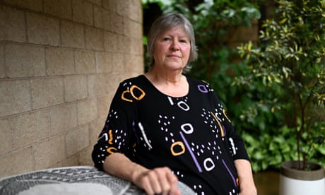 Woman wearing black dress with coloured shapes sits on outdoor furniture in a house garden