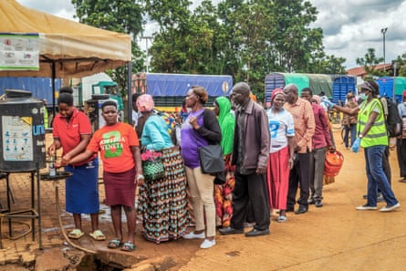 People queue to wash their hands at an outdoor tap.