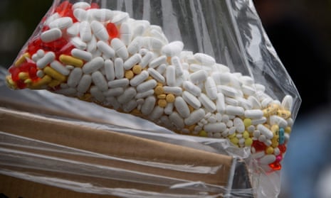 A large plastic bag of various pills sits in a box.