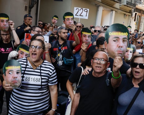 Protesters hold masks depicting Valencia's regional President Carlos Mazón.