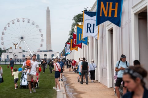 crowd of people stand outside by monuments and flags of each US state, a ferris wheel in background