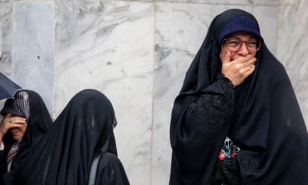 Women in dark clothes, with one of them apparently in tears, on a street