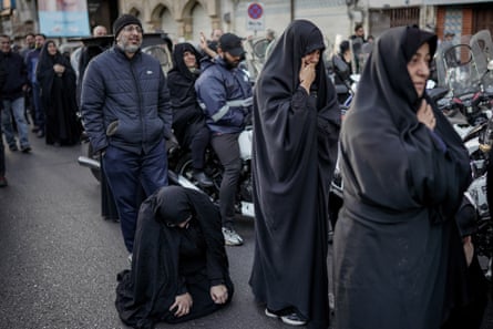 Men and women weep in the street, including one woman kneeling on the road with head bowed