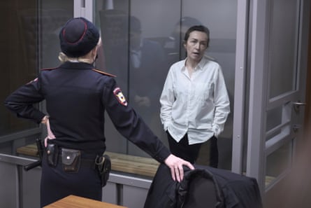 A woman stands behind glass in a courtroom as a policewoman