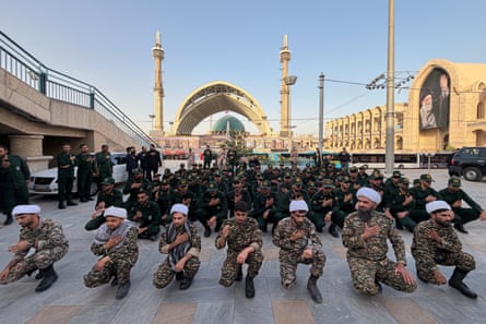 People kneel facing the camera, with the mosque behind