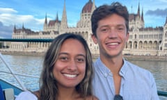 A man and woman - a couple - pose for a photo on a boat, with a Budapest castle in the background.