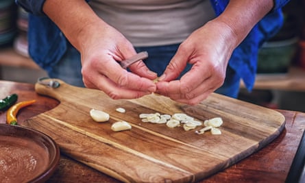 A person chops garlic on a wooden board.