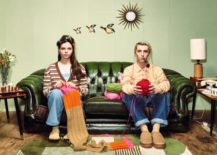 Young couple sitting on a sofa as if they’re old people, her knitting, rollers in her hair, him holding a ball of wool, flying ducks behind them on the wall
