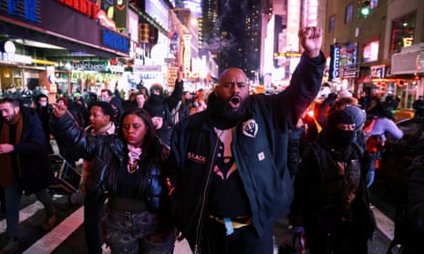 A group of protestors, some with raised fists, march through a brightly lit street in Times Square. 