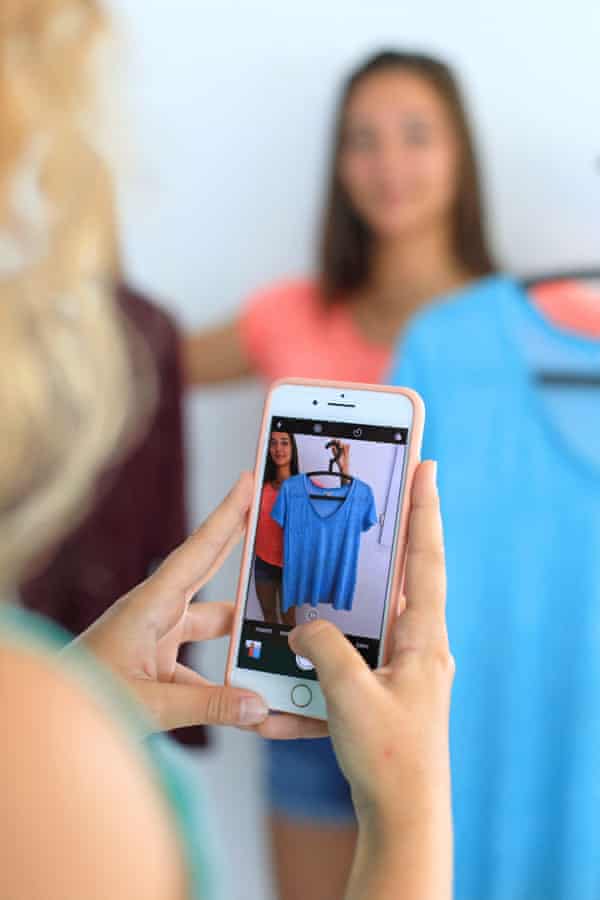 A teenager uses her phone to photograph a piece of clothing being held up by her friend for a secondhand clothes app