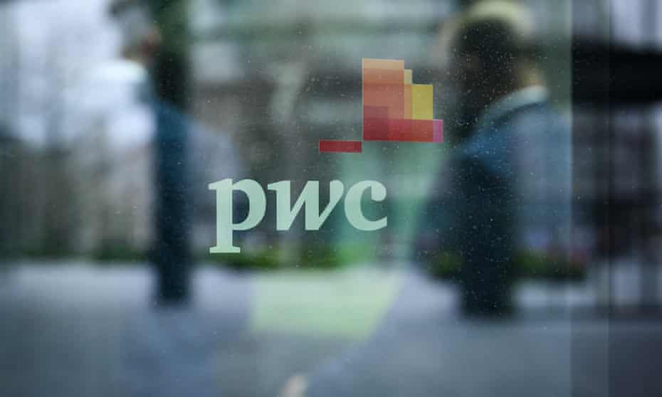 People walk past a sign on a window on the exterior of the PWC London offices in London