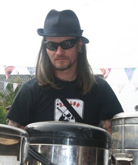 Mark, unsmiling with long hair, wears a fedora, black skull t-shirt and sunglasses