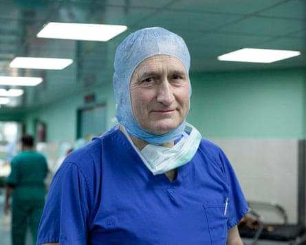 Surgeon in royal blue scrubs and blue hair covering.