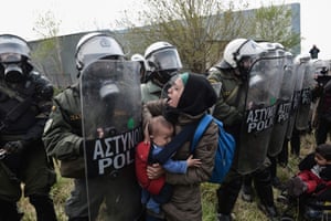 Une femme tient un enfant devant la police anti-émeute grecque devant un camp de réfugiés près de Thessalonique.